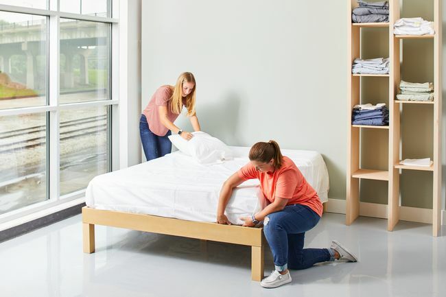 dve ženy ustlávajú posteľ s bielymi plachtami